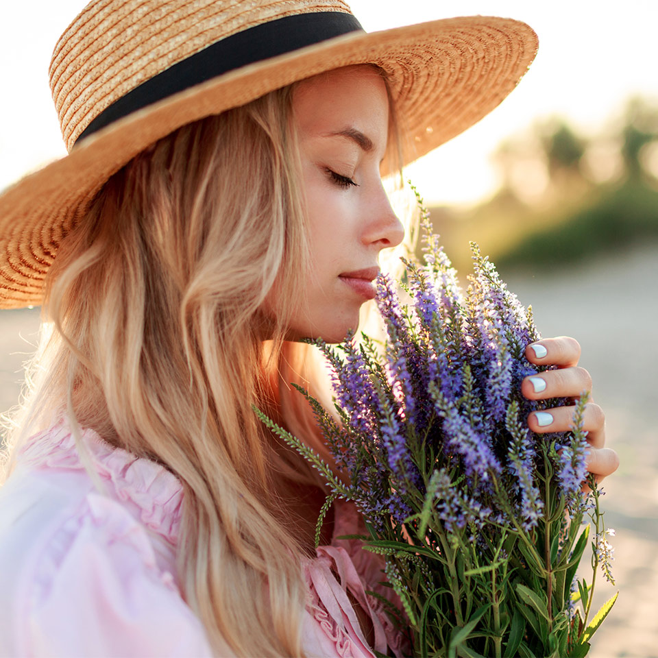 Woman in straw hat smelling flowers, the sun is setting behind her
