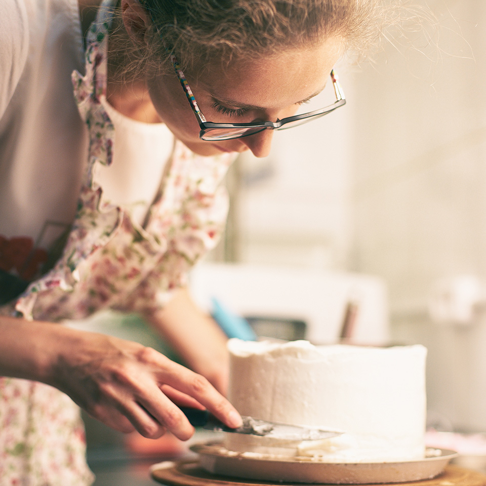 Woman wearing an apron, decorating a cake