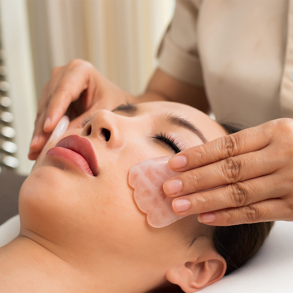 Reflexologist using Gua Sha massage tools on a woman’s face