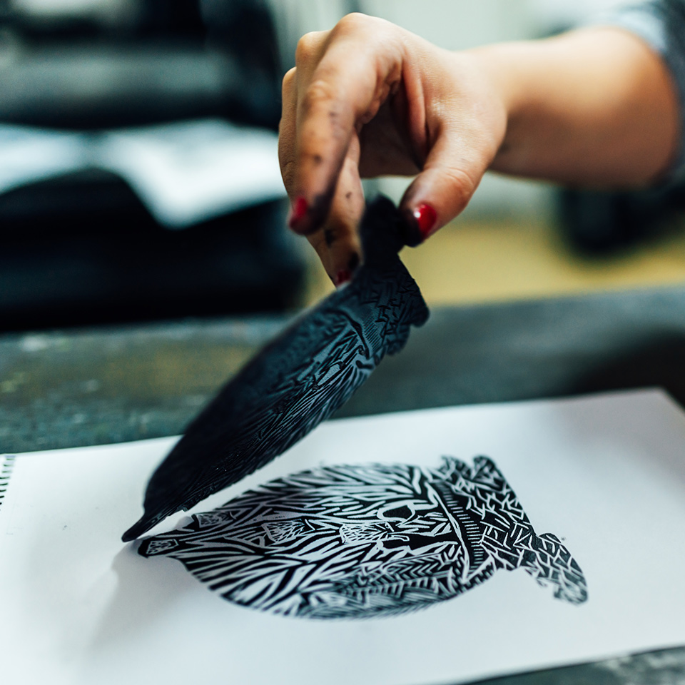 Artist lifting a piece of carved lino, leaving a patterned print on the page