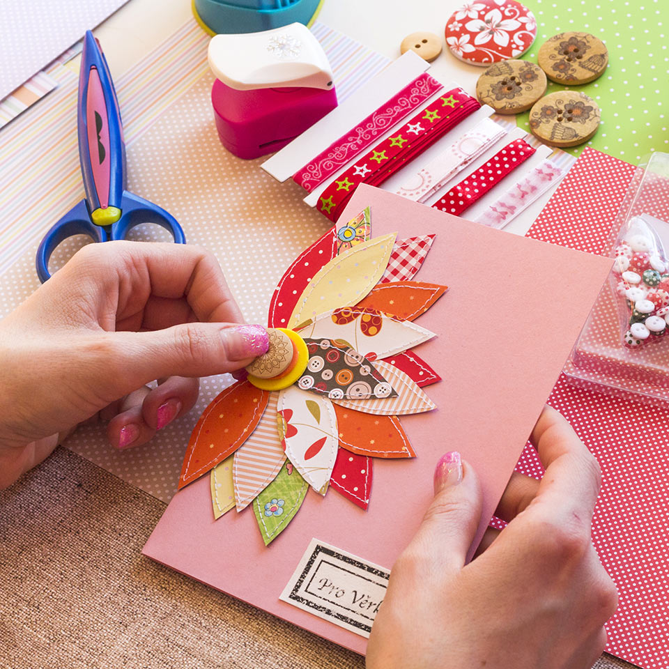 Hands making a handmade card with a fabric and button flower on it